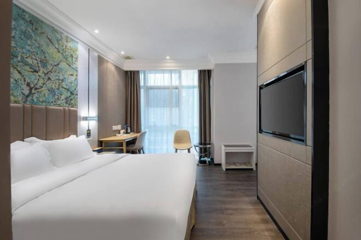 Hotellihuone, jossa on sänky, työpöytä, tuoli, televisio ja suuri ikkuna.