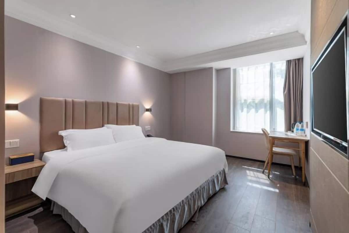 Hotellihuone, jossa on suuri sänky, yöpöydät, työpöytä ja ikkuna, jossa on verhot.