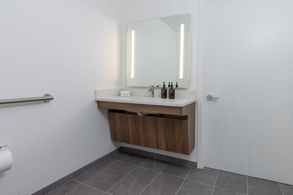 A modern bathroom with a white sink, wooden cabinet, and a large mirror. - Kasa Little Italy San Diego (San Diego)