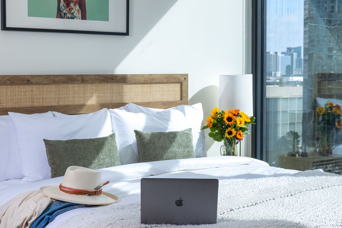 Een net opgemaakt bed met een laptop, koffer en hoed erop.