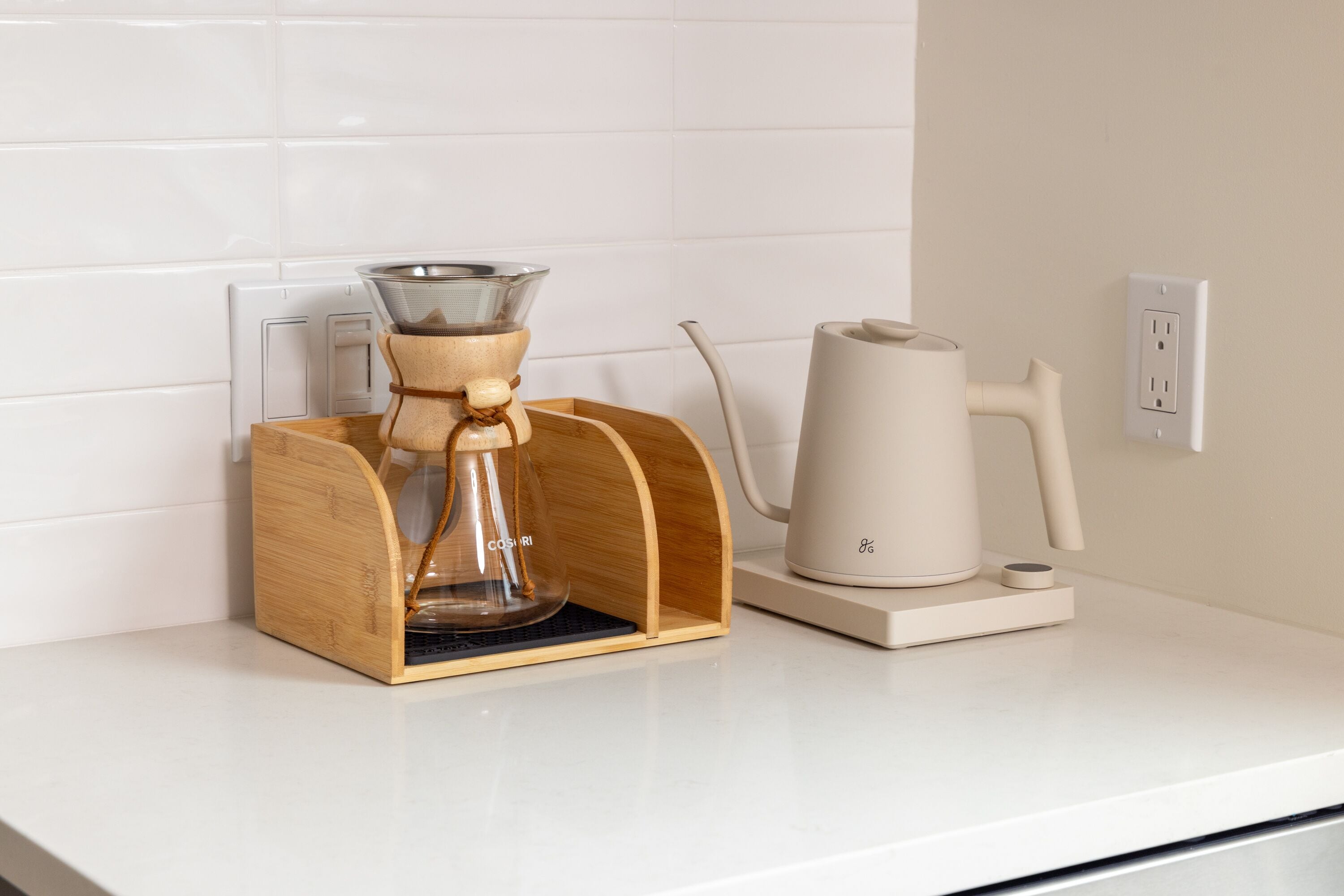 A coffee maker and a kettle on a white countertop with a wooden coffee pod holder.