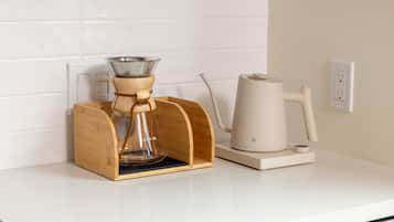 A coffee maker and a kettle on a white countertop with a wooden coffee pod holder.