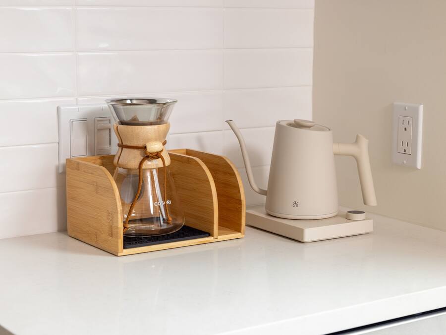 A coffee maker and a kettle on a white countertop with a wooden coffee pod holder.