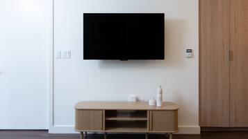 A modern living room with a mounted flat-screen TV, a wooden cabinet with two shelves, and a wooden wardrobe.