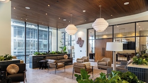 Eine moderne Lobby mit Sitzbereichen, großen Fenstern und Zimmerpflanzen.