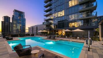 A rooftop pool with lounge chairs and umbrellas, surrounded by modern buildings.