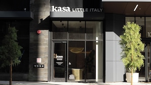 Ein modernes Gebäude mit einem Schild, auf dem "kasa little Italy" steht, und einem Glastür-Eingang.
