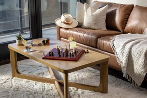 A cozy living room with a leather sofa, a wooden coffee table with a chessboard, a small plant, and a drink on the table.