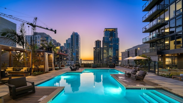 Ein Pool auf dem Dach mit Liegestühlen und einer Stadtkulisse im Hintergrund.