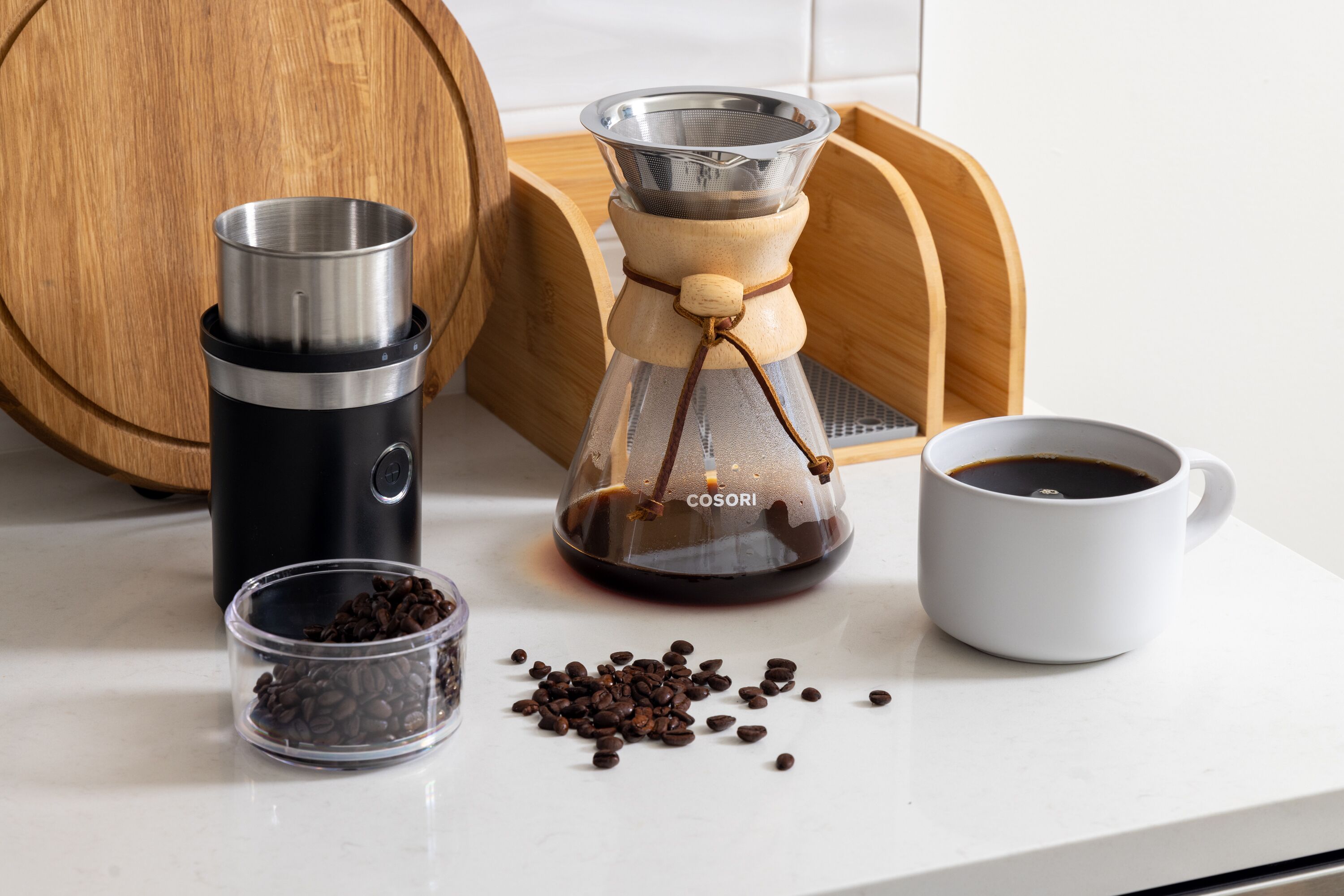Una cafetera, una taza de café y un molinillo de café sobre una encimera de cocina.