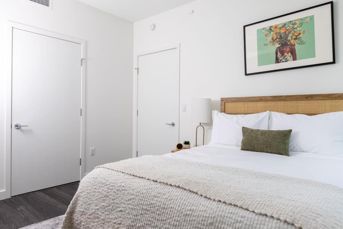 Een slaapkamer met een bed, hoofdeinde, een lijst met foto aan de muur en een deur.