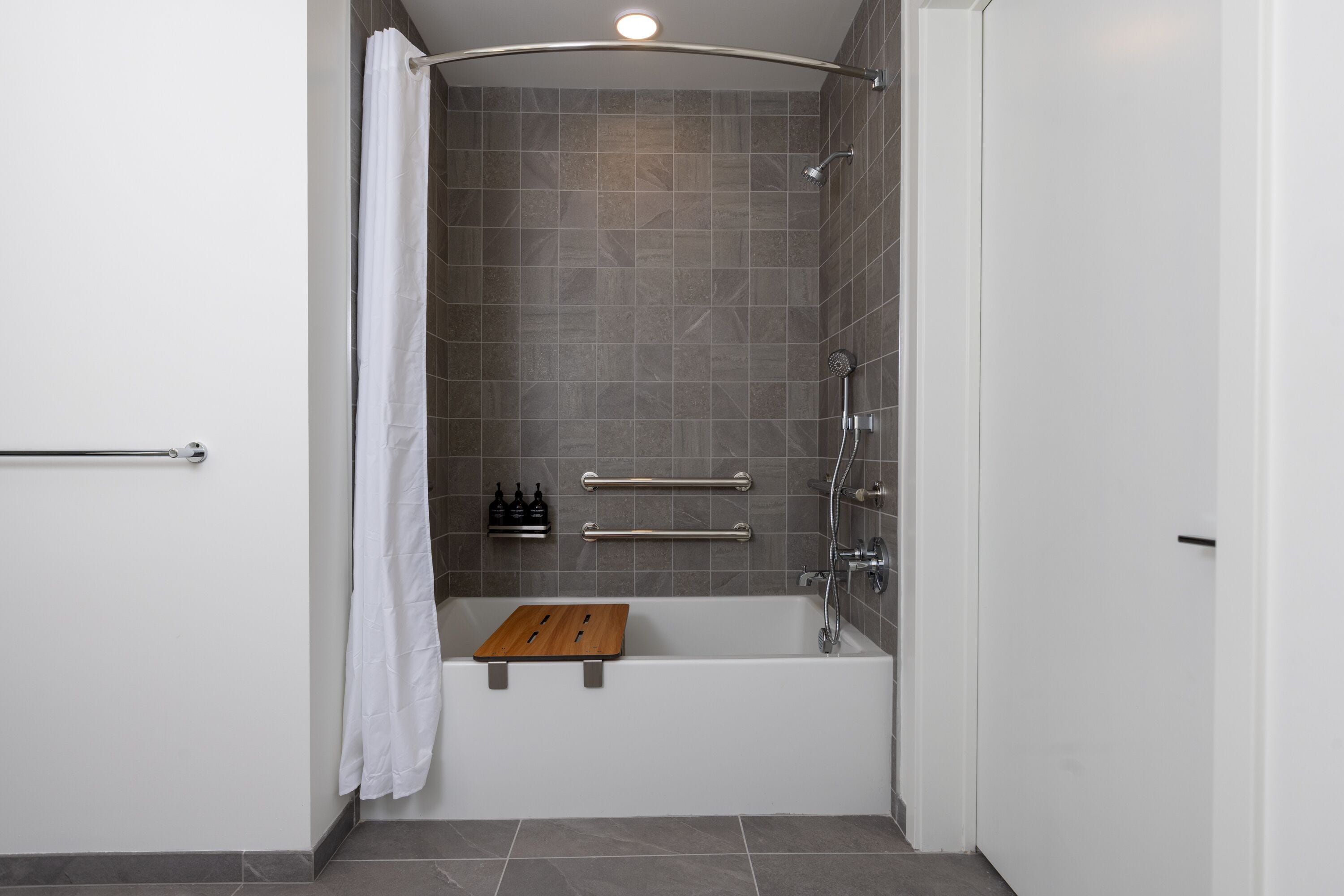 A modern bathroom with a bathtub, shower, and grab bars.