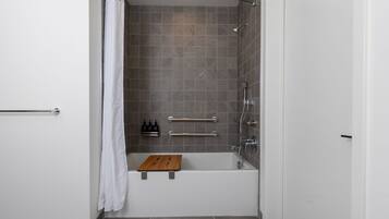 A modern bathroom with a bathtub, shower, and grab bars.