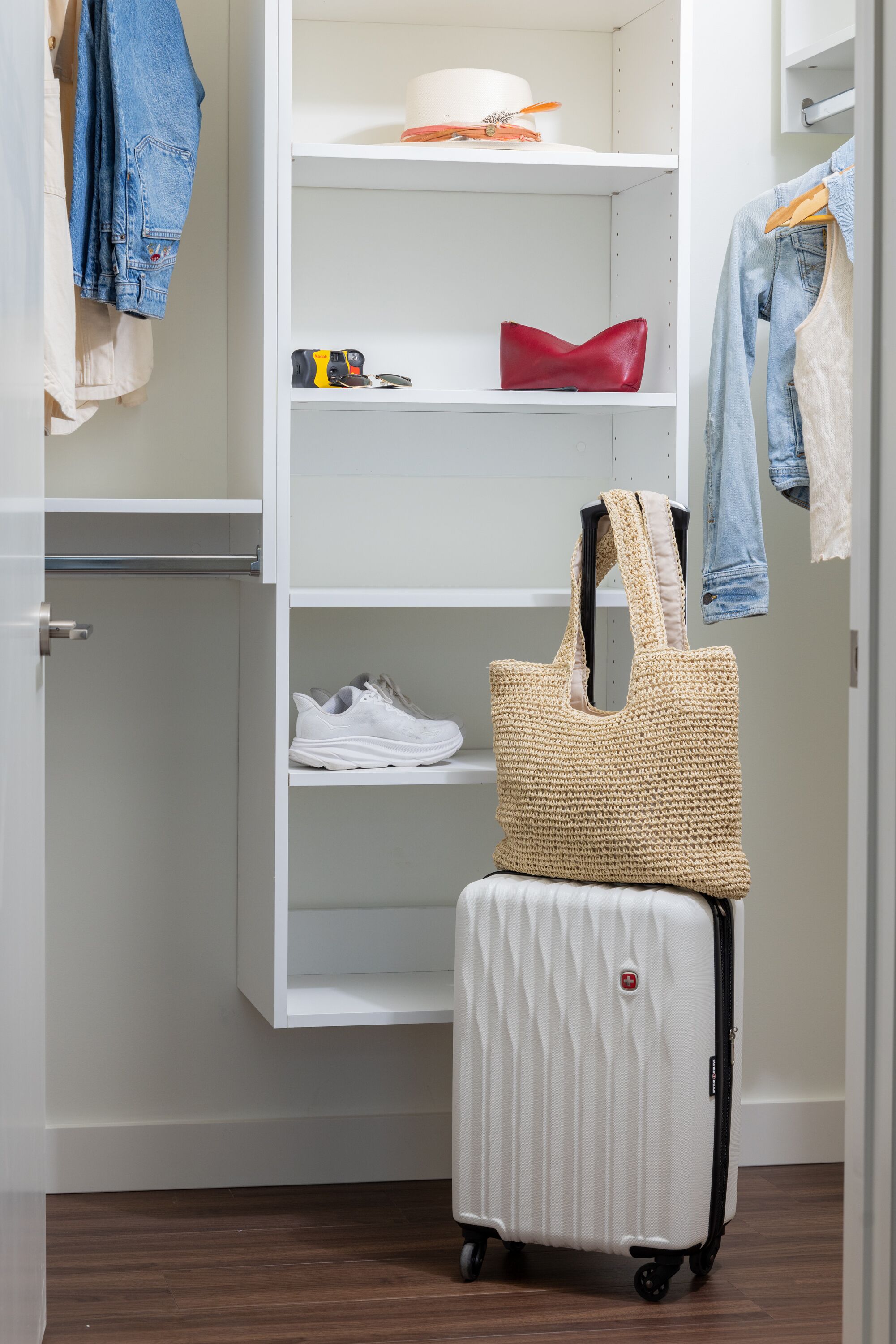 A white wardrobe with shelves, a hanging bag, and a suitcase.
