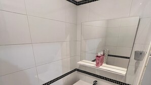 A bathroom with white tiles, a white sink, a mirror, and a toilet. - Newly Renovated Gem: 15 mins train ride to Paris (Sarcelles)