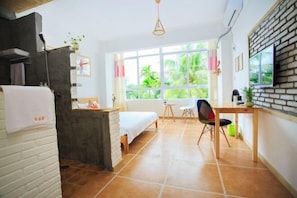 A compact hotel room with a bed, a small desk, a chair, and a window with a view of greenery. - Sanya Sunflower Coast Inn (Sanya)