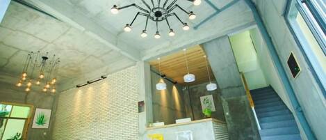 A modern interior with a reception desk, seating area, staircase, and a unique ceiling light fixture.