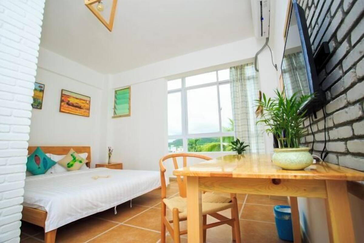 Ein Schlafzimmer mit einem Bett, einem Holztisch und einem Fenster mit Blick auf Grünflächen.