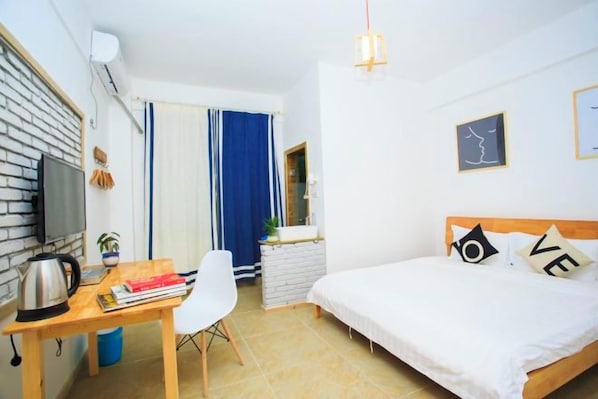 A hotel room with a bed, a desk with a kettle, a chair, a television, and a window with curtains.