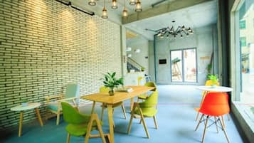 A modern interior with a brick wall, a wooden table, green chairs, and a bright orange chair.