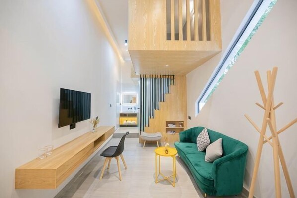 Una sala moderna con un sofá verde, un mueble de televisión de madera, una mesita y una escalera que lleva a un nivel superior.