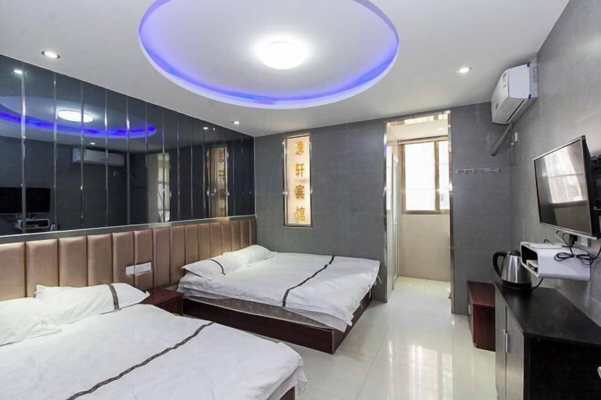 A hotel room with two beds, a large mirror, a flat-screen TV, and a wall-mounted air conditioner.