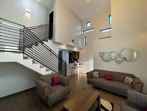 Stylish living space with a central staircase, sofa, armchairs, and a coffee table.