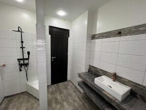 Modern bathroom with a white tiled shower, handheld showerhead, and a sink with a countertop.