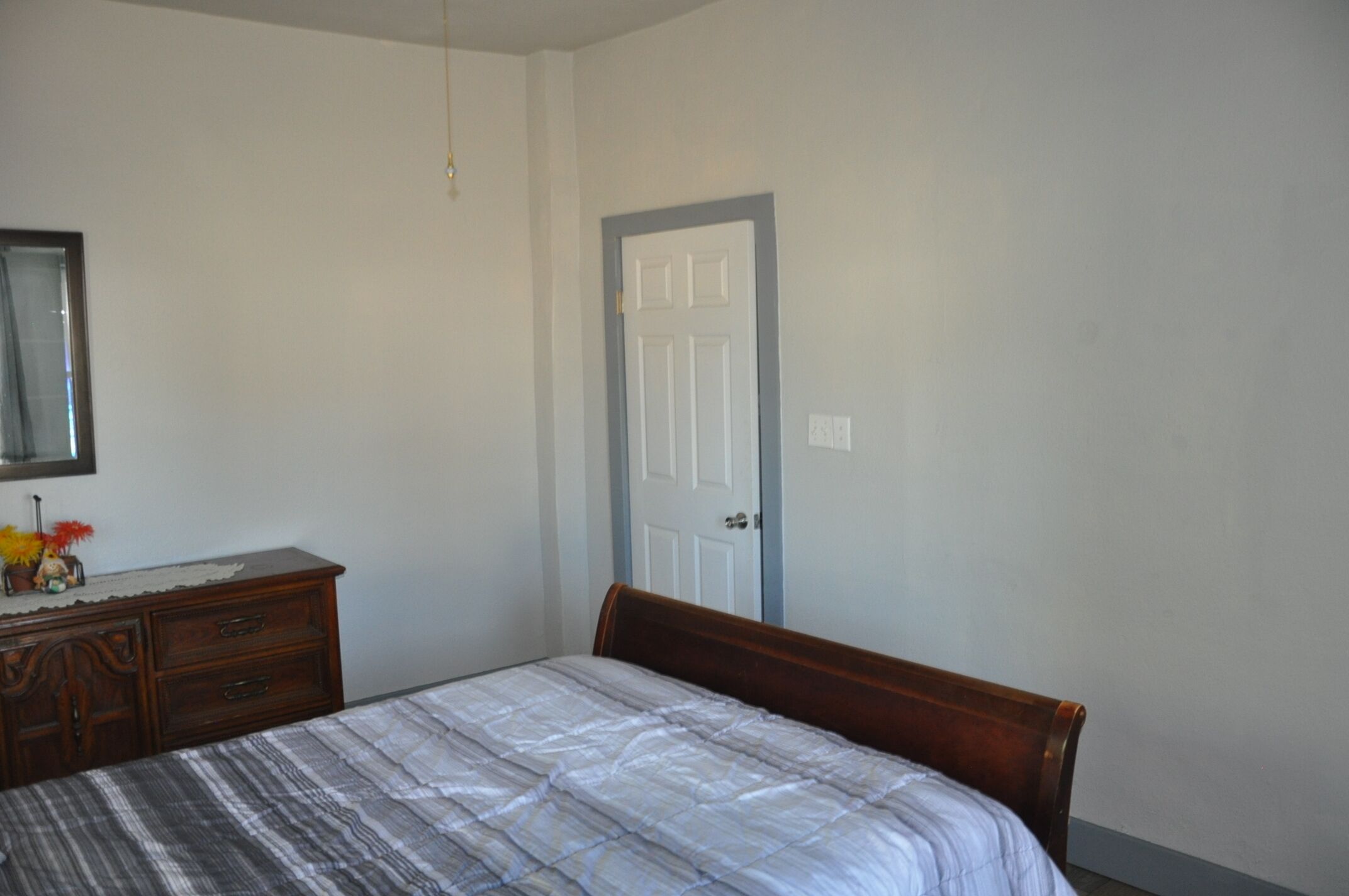 A bedroom with a bed, a dresser, a mirror, and a door.