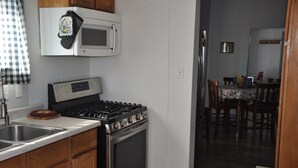 Una cocina con estufa, microondas y pileta. Se observa un comedor con una mesa y sillas al fondo.