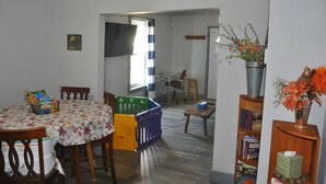 Comedor con mesa, sillas, una pequeña alberca para bebés, estantería y ventana con cortinas.
