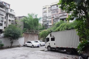 Un edificio residencial de varios pisos con un coche blanco y una camioneta blanca estacionados en una calle estrecha.