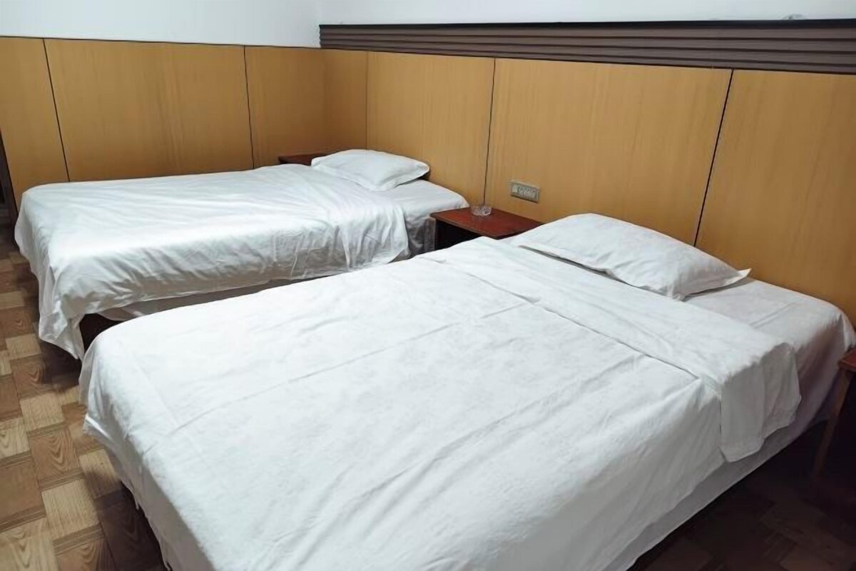 Quarto de hotel com duas camas de solteiro, cabeceira de madeira e uma pequena mesa de cabeceira.