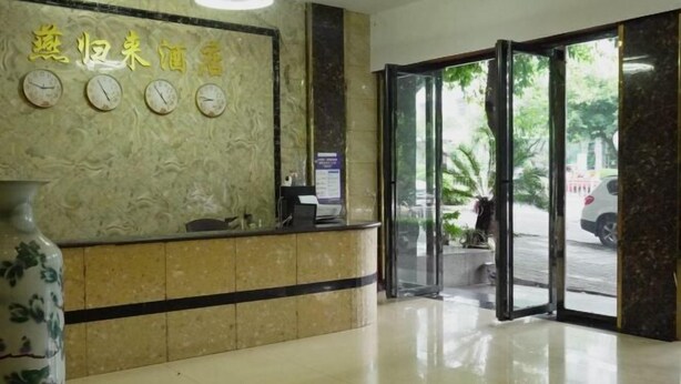 A hotel reception area with a marble wall, a reception desk, and a large vase. - Changning Yanyi Hotel (Changning)