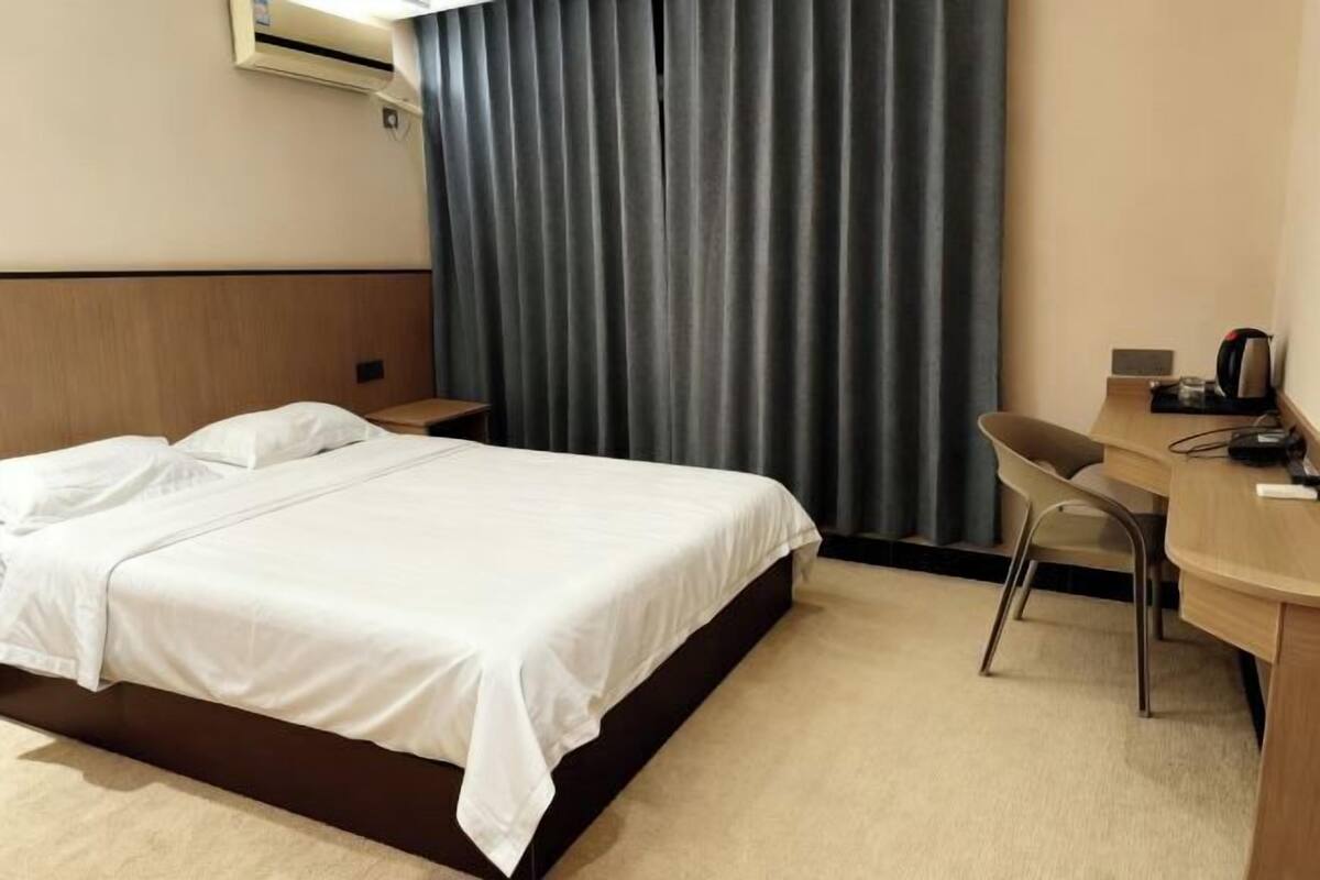 Hotellihuone, jossa on sänky, työpöytä, tuoli, kahvinkeitin ja verho.