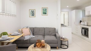 Un salon moderne avec un canapé gris, une table à manger avec des assiettes et des bols blancs, et une petite table ronde agrémentée d’objets décoratifs.