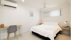 A bedroom with a bed, bedside tables, a desk, a chair, an air conditioner, a ceiling fan, and a window with blinds. - 1 Bdr Apt w/ AC & Kitchen | Parking | 135F1 (Rocklea)
