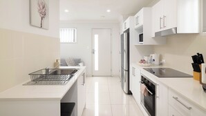 A modern kitchen with white cabinets, a stainless steel refrigerator, and a black oven. - 1 Bdr Apt w/ AC & Kitchen | Parking | 135F1 (Rocklea)