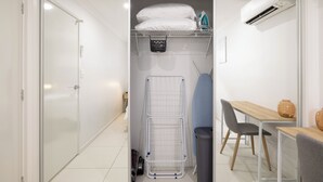 A compact, modern room with a built-in wardrobe, a drying rack, a small table with a vase, and a trash bin. - 1 Bdr Apt w/ AC & Kitchen | Parking | 135F1 (Rocklea)