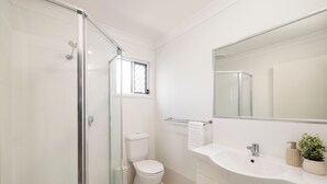 Un baño moderno con cabina de ducha de vidrio, inodoro y lavabo con espejo.