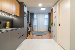 Um corredor estreito com uma área de cozinha de um lado, apresentando armários modernos e um forno embutido.