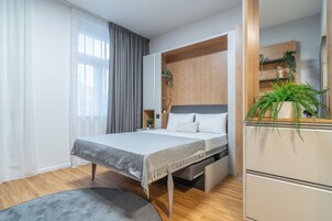Ein modernes Schlafzimmer mit Bett, integrierten Stauraumlösungen, einem Nachttisch und einem großen Fenster mit Vorhängen.