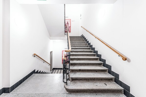 A staircase with black and white tiles, wooden handrails, and a red emergency exit sign. - City Pop 2Night Prague - Self check-in (Prague)