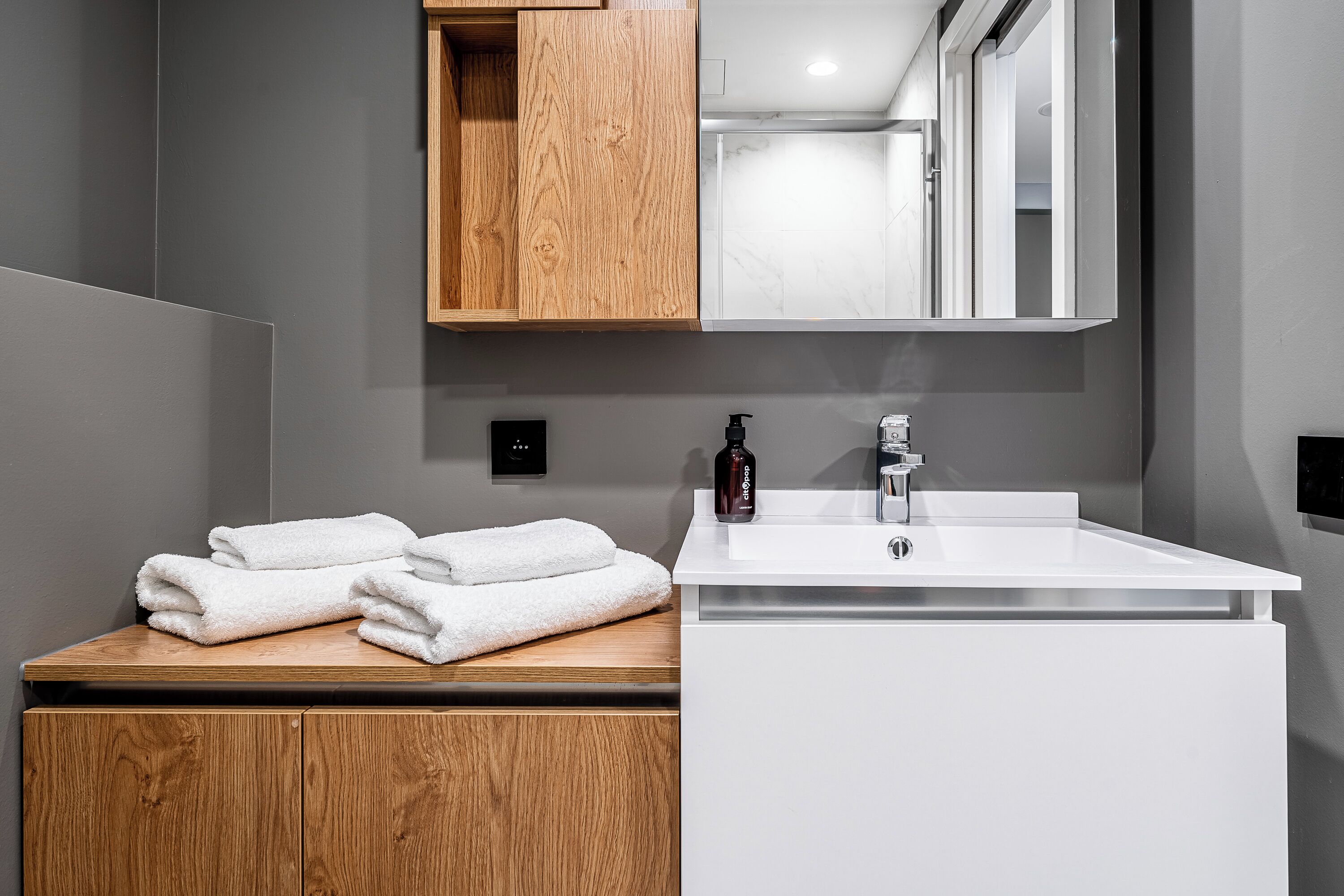 A modern bathroom with a wooden vanity, white sink, and a mirror above the sink.