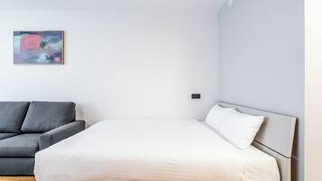 Ein modernes Schlafzimmer mit einem Bett, einem grauen Sofa und einem minimalistischen abstrakten Gemälde an der Wand.