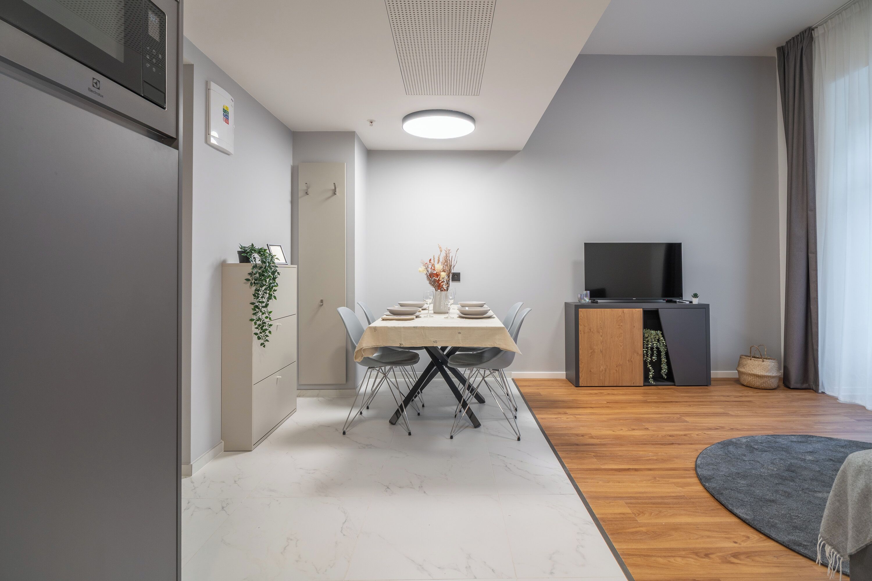 A modern living room with a dining area, a flat-screen TV, and a wooden cabinet.