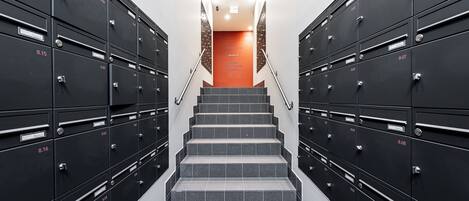 A set of black metal lockers with numbered labels, arranged in two rows on either side of a staircase leading to an orange door.