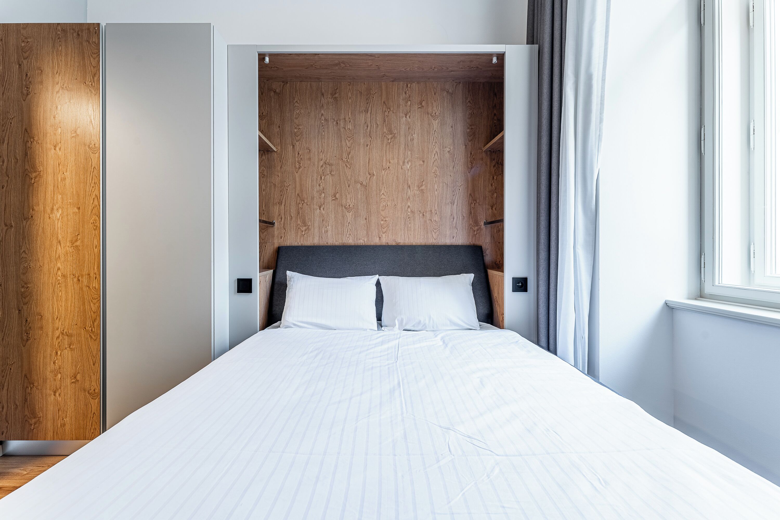 A bedroom with a bed, wooden wardrobe, and a window.