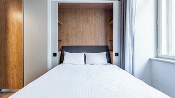A bedroom with a bed, wooden wardrobe, and a window.