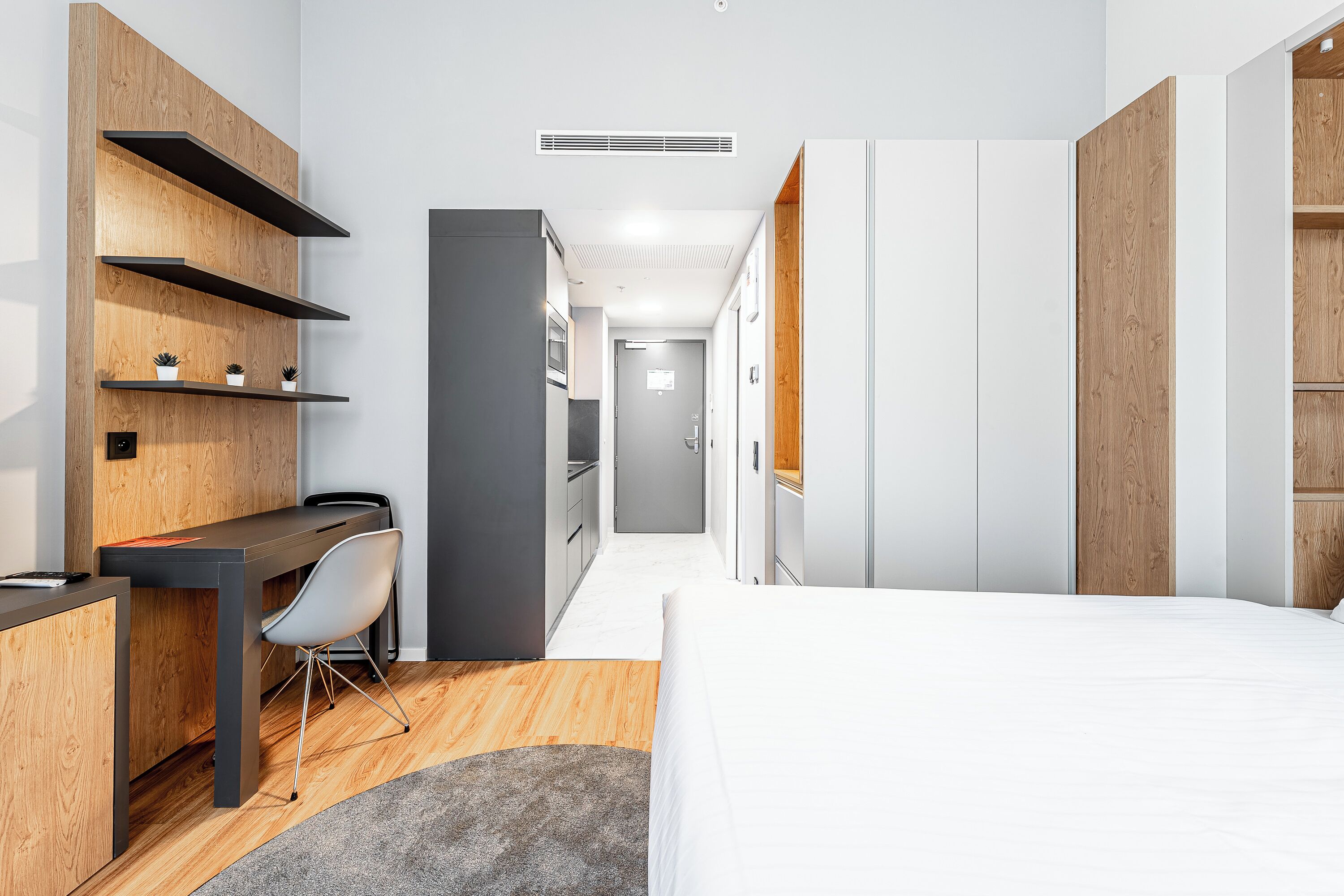 Una moderna camera d'hotel con una scrivania in legno, una sedia, un letto e scaffali a muro.